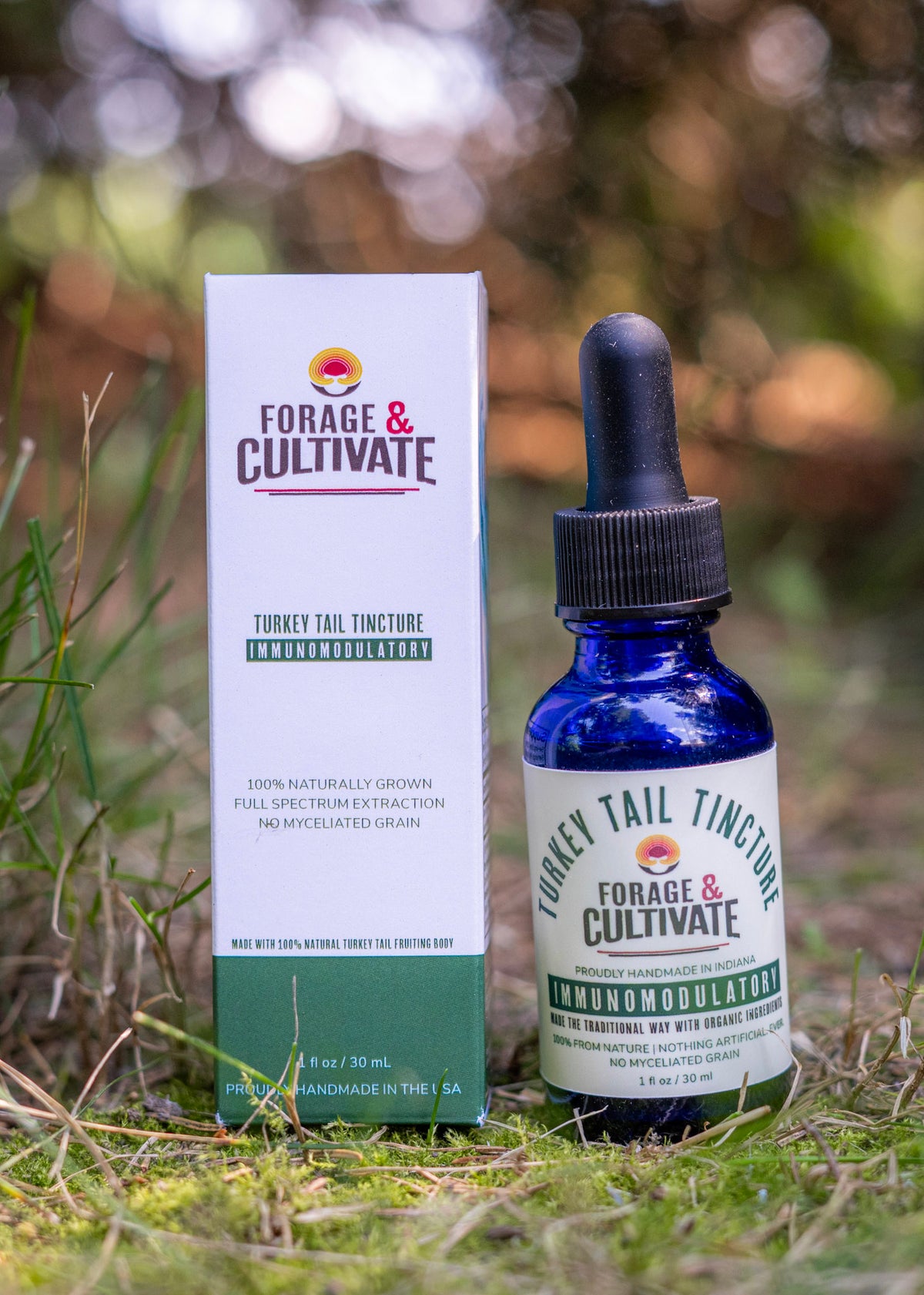 A bottle of Forage & Cultivate Turkey Tail Tincture next to its retail box, placed on grass outdoors with a blurred natural background.